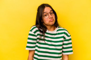 Sarı arka planda izole edilmiş genç İspanyol kadın omuzlarını silker ve gözleri açık kalır..