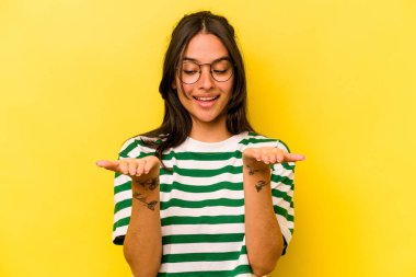 Sarı arka planda izole edilmiş genç İspanyol kadın elinde avuç içi bir şeyle kameraya sunuyor..