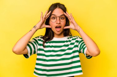 Sarı arka planda izole edilmiş genç İspanyol kadın hoş bir sürprizle karşılaşıyor, heyecanlı ve el kaldırıyor..