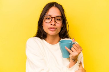 Sarı arka planda izole edilmiş bir kupa tutan genç İspanyol kadın.