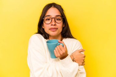 Sarı arka planda izole edilmiş bir kupa tutan genç İspanyol kadın.