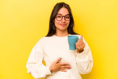 Sarı arka planda izole edilmiş bir kupa tutan genç İspanyol kadın.