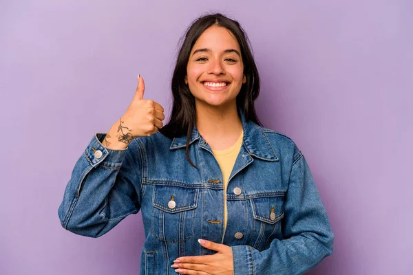 Mor arka planda izole edilmiş genç İspanyol kadın karnına dokunuyor, nazikçe gülümsüyor, yemek yiyor ve tatmin oluyor..