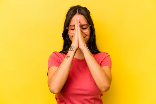 若いヒスパニック系の女性が黄色の背景に手を握って口の近くに祈るに隔離され 自信を感じる — ストック写真