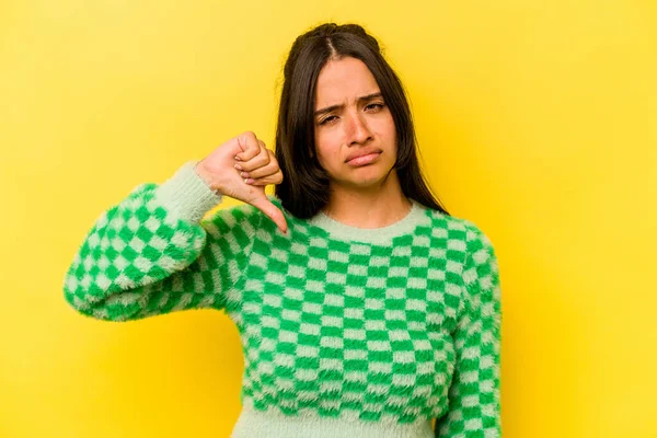 Sarı arka planda izole edilmiş genç İspanyol kadın baş parmağını aşağı gösteriyor, hayal kırıklığı konsepti..
