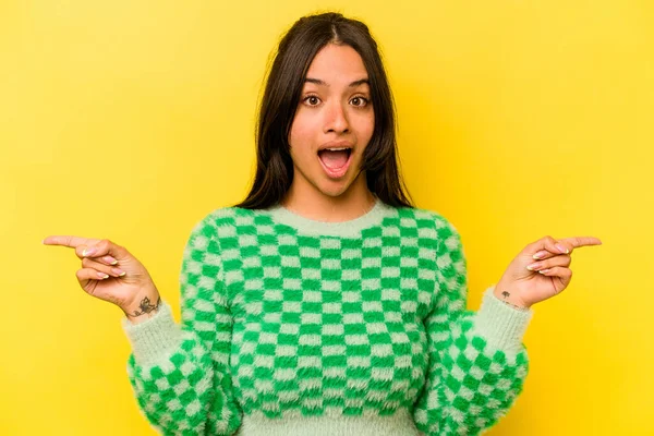 Sarı arka planda izole edilmiş genç İspanyol kadın farklı kopya alanlarını gösteriyor, birini seçiyor, parmaklarıyla gösteriyor.