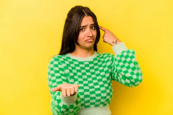 Sarı arka planda izole edilmiş genç İspanyol kadın elinde bir ürün tutuyor..