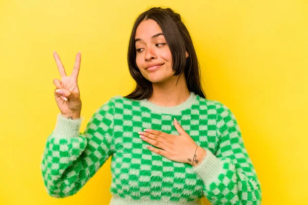 Sarı arka planda izole edilmiş genç İspanyol kadın yemin ediyor, elini göğsüne koyuyor..