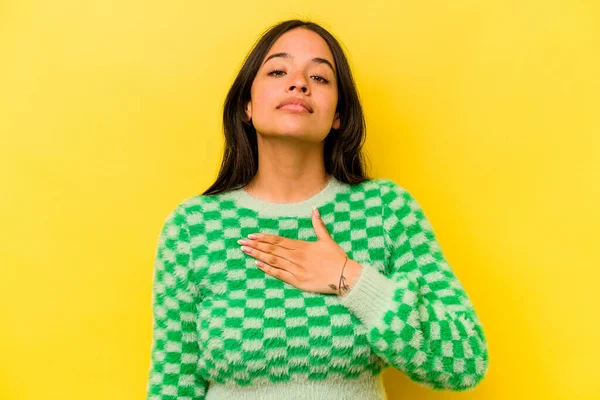 Sarı arka planda izole edilmiş genç İspanyol kadın yemin ediyor, elini göğsüne koyuyor..