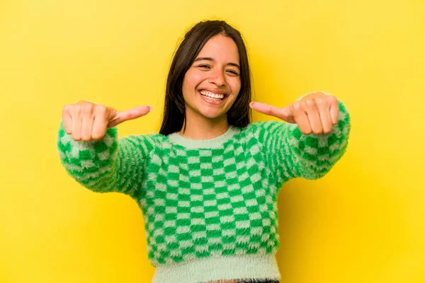 Sarı arka planda izole edilmiş genç İspanyol kadın iki parmağını da kaldırıyor, gülümsüyor ve kendinden emin..