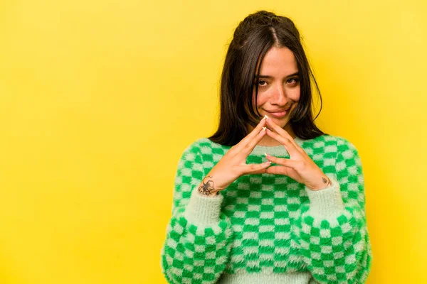 Latin kökenli genç bir kadın sarı arka planda izole edilmiş bir plan kuruyor, bir fikir kuruyor..