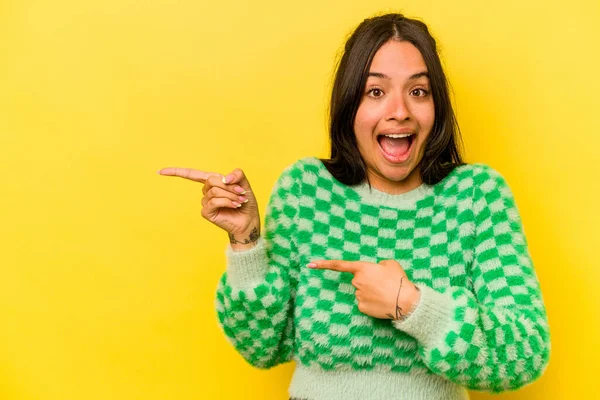 Sarı arka planda izole edilmiş genç İspanyol kadın işaret parmağıyla işaret ettiği için heyecanlı..