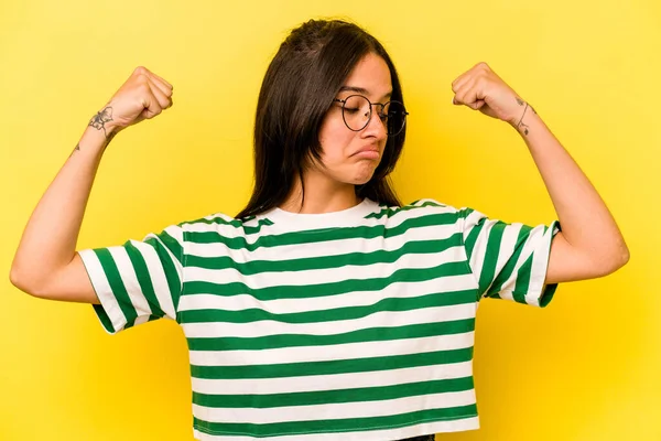 Sarı arka planda izole edilmiş genç İspanyol kadın güçlü hareketlerini kollarıyla gösteriyor, kadın gücünün sembolü.