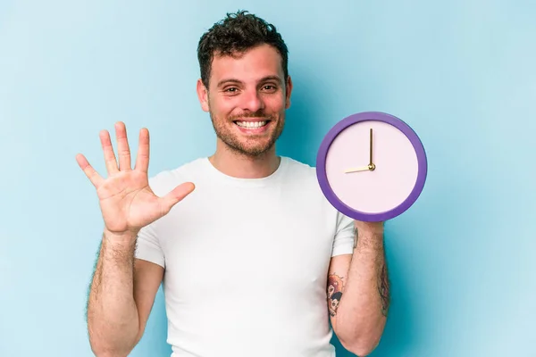 Young Caucasian Man Holding Clock Isolated Blue Background Smiling Cheerful — Stock Fotó