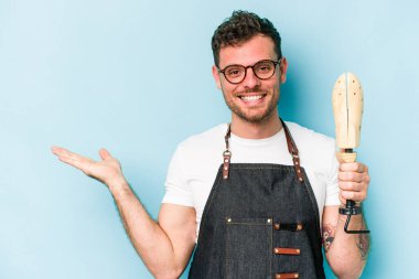 Kafkasyalı genç kunduracı mavi arka planda izole edilmiş bir şekilde bir palmiye üzerinde fotokopi alanı ve belinde bir el daha gösteriyor..