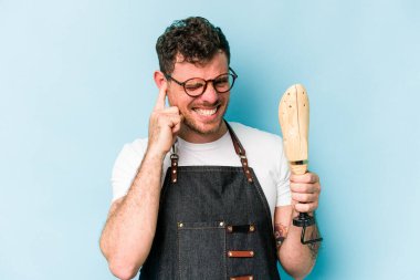 Kafkasyalı genç kunduracı, mavi arka planda izole edilmiş kulakları elleriyle kapatıyor..