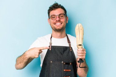 Kafkasyalı genç kunduracı, mavi arka planda izole edilmiş, gömlekli bir fotokopiciyi işaret ediyor, gururlu ve kendinden emin.