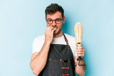 Kafkasyalı genç kunduracı, mavi arka planda izole edilmiş tırnak yiyor, gergin ve endişeli..