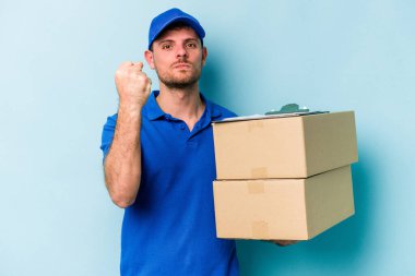 Mavi arka planda izole edilmiş genç beyaz teslimatçı kameraya yumruk gösteriyor, agresif yüz ifadesi var..