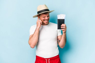 Pasaportu elinde tutan Kafkasyalı genç adam mavi arka planda izole edilmiş kulakları elleriyle kapatıyor..