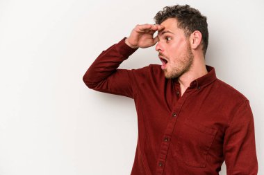 Beyaz arka planda izole edilmiş genç beyaz bir adam uzaklara bakıyor ve elini alnına koyuyor..