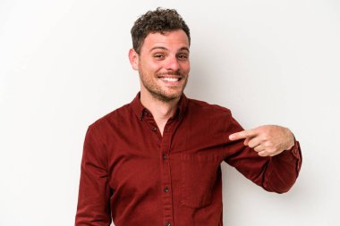 Beyaz arka planda yaşayan beyaz tenli genç bir adam gömlek fotokopi alanını gösteriyor, gururlu ve kendinden emin.