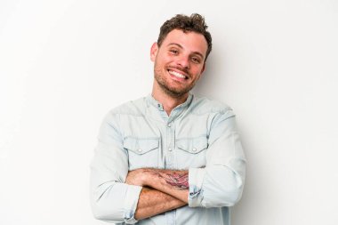 Beyaz arka planda kendini güvende hisseden, kararlılıkla kollarını kavuşturan beyaz tenli genç bir adam..