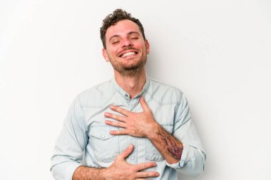 Beyaz arka planda izole genç beyaz adam mutlu bir şekilde gülüyor ve ellerini karnının üstünde tutarak eğleniyor..