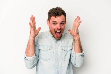 Beyaz arka planda izole olmuş genç beyaz bir adam zaferi veya başarıyı kutluyor, şaşırıyor ve şok oluyor..