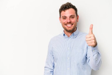 Beyaz arka planda izole edilmiş genç beyaz adam gülümsüyor ve başparmağını kaldırıyor.