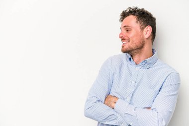 Beyaz arka planda izole edilmiş genç beyaz adam kollarını kavuşturarak gülümsüyor..