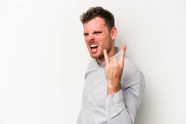 Beyaz arka planda izole edilmiş genç beyaz bir adam parmaklarıyla kaya hareketi gösteriyor.