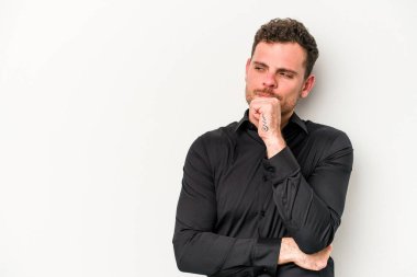 Beyaz arka planda izole edilmiş genç beyaz bir adam şüpheli ve şüpheci bir ifadeyle yana bakıyor..