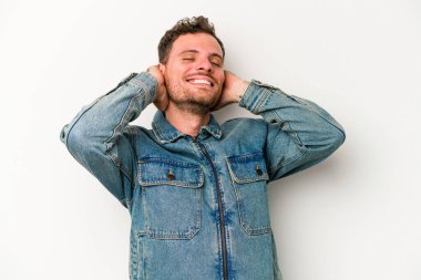 Beyaz arka planda izole olmuş genç beyaz bir adam kendini güvende hissediyor, elleri başının arkasında..