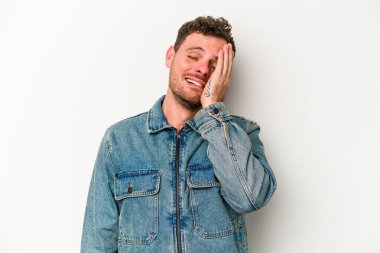 Beyaz arka planda izole edilmiş genç beyaz bir adam yorgun ve uykulu bir şekilde elini başının üstünde tutuyor..