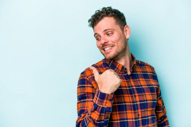 Kafkasyalı genç adam mavi arka plan noktalarında izole edilmiş başparmak uzakta, gülüyor ve kaygısız.