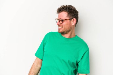 Beyaz arka planda izole edilmiş genç beyaz adam gevşemiş ve mutlu bir şekilde gülüyor, boynunda dişlerini gösteriyor..