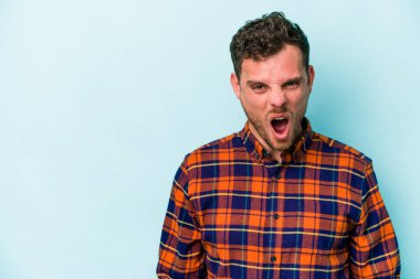 Kafkasyalı genç adam mavi arka planda izole edilmiş. Çok kızgın, öfkeli, hayal kırıklığına uğramış..