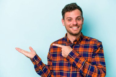 Kafkasyalı genç adam mavi arka planda izole edilmiş. Elinde palmiye ağacının bir kopyası olduğu için heyecanlı..