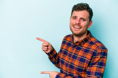 Mavi arka planda izole edilmiş genç beyaz adam işaret parmağıyla fotokopi alanını işaret ederek şok oldu..