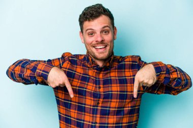 Kafkasyalı genç adam mavi arka planda izole edildi. Parmakları aşağıda, olumlu bir his var..