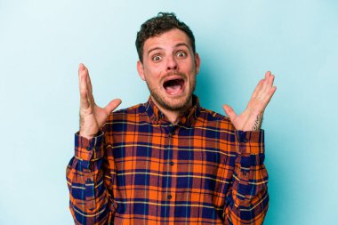 Kafkasyalı genç adam mavi arka planda izole edilmiş gökyüzüne haykırıyor, yukarı bakıyor, hayal kırıklığına uğramış..