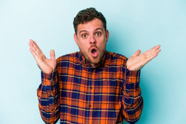 Kafkasyalı genç adam mavi arka planda izole edildi. Şaşırdı ve şok oldu..