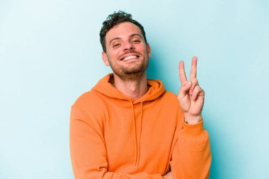 Mavi arka planda izole edilmiş genç beyaz adam iki numarayı parmaklarıyla gösteriyor..