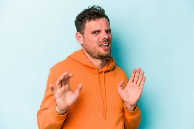 Mavi arka planda izole edilmiş genç beyaz adam tiksinti belirtisi gösteren birini reddediyor..