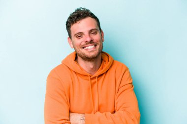 Kafkasyalı genç adam mavi arka planda izole edilmiş gülüyor ve eğleniyor..