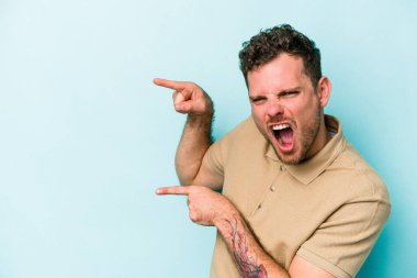 Kafkasyalı genç adam mavi arka planda izole edilmiş. İşaret parmağıyla işaret ettiği için heyecanlı..