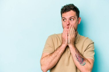 Kafkasyalı genç adam mavi arka planda izole edilmiş. Düşünceli bir şekilde ağzıyla ağzını kapatan bir fotokopi odasına bakıyor..