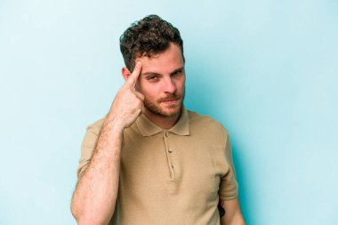 Mavi arka planda izole edilmiş genç beyaz bir adam şakağı parmağıyla işaret ediyor, düşünüyor ve bir göreve odaklanıyor..