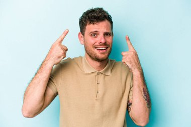 Mavi arka planda izole edilmiş genç beyaz adam işaret parmağıyla bir hayal kırıklığı jesti gösteriyor..